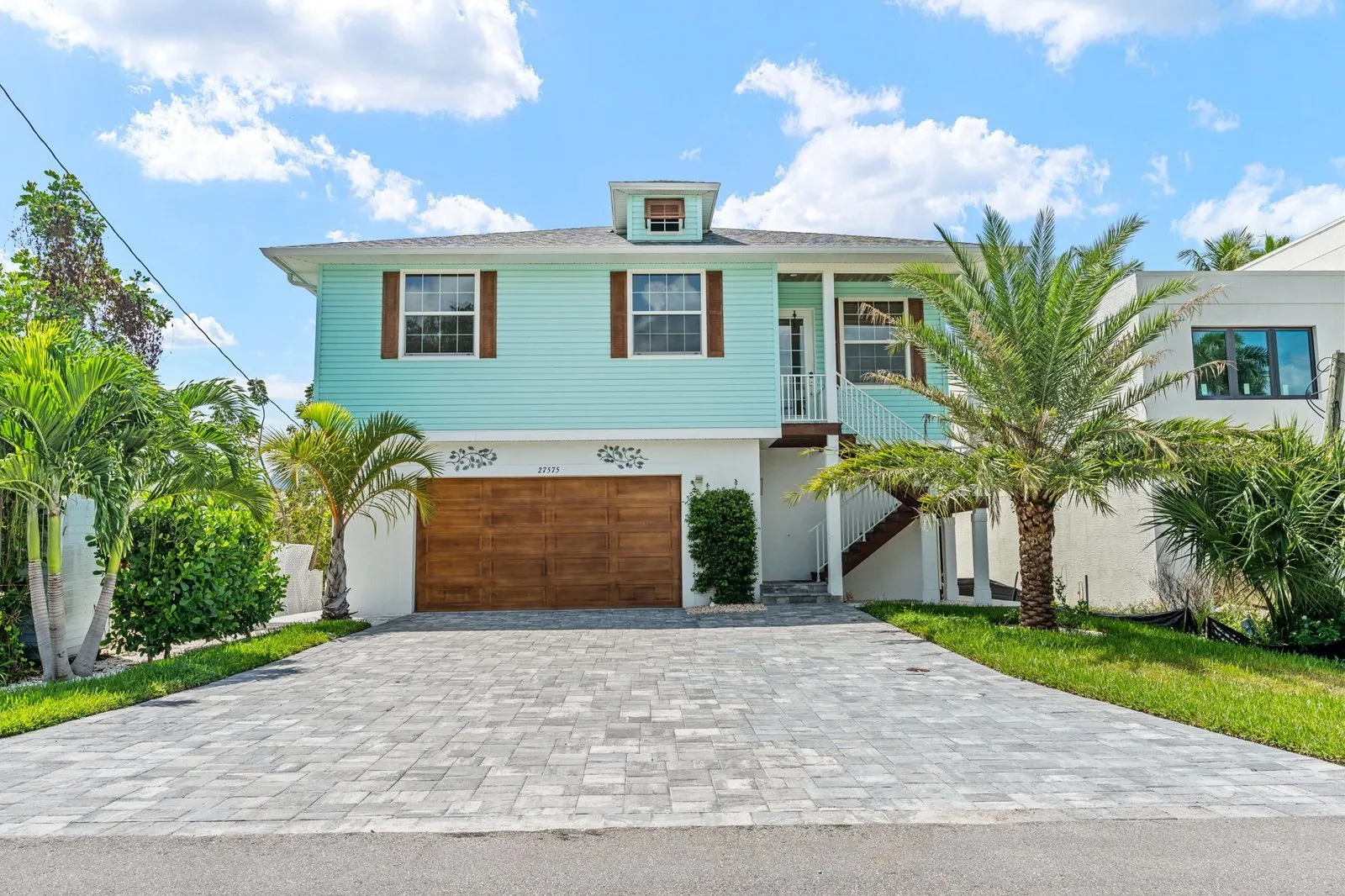 Front of a turquoise two-story coastal home with palm trees and a paver driveway