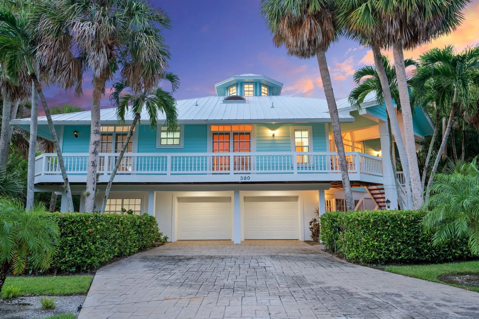 Raised coastal home with palms and a three-car garage