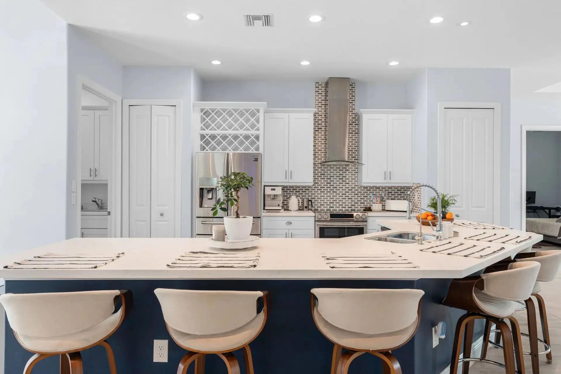 White kitchen with a long island, bar stools and a wine display