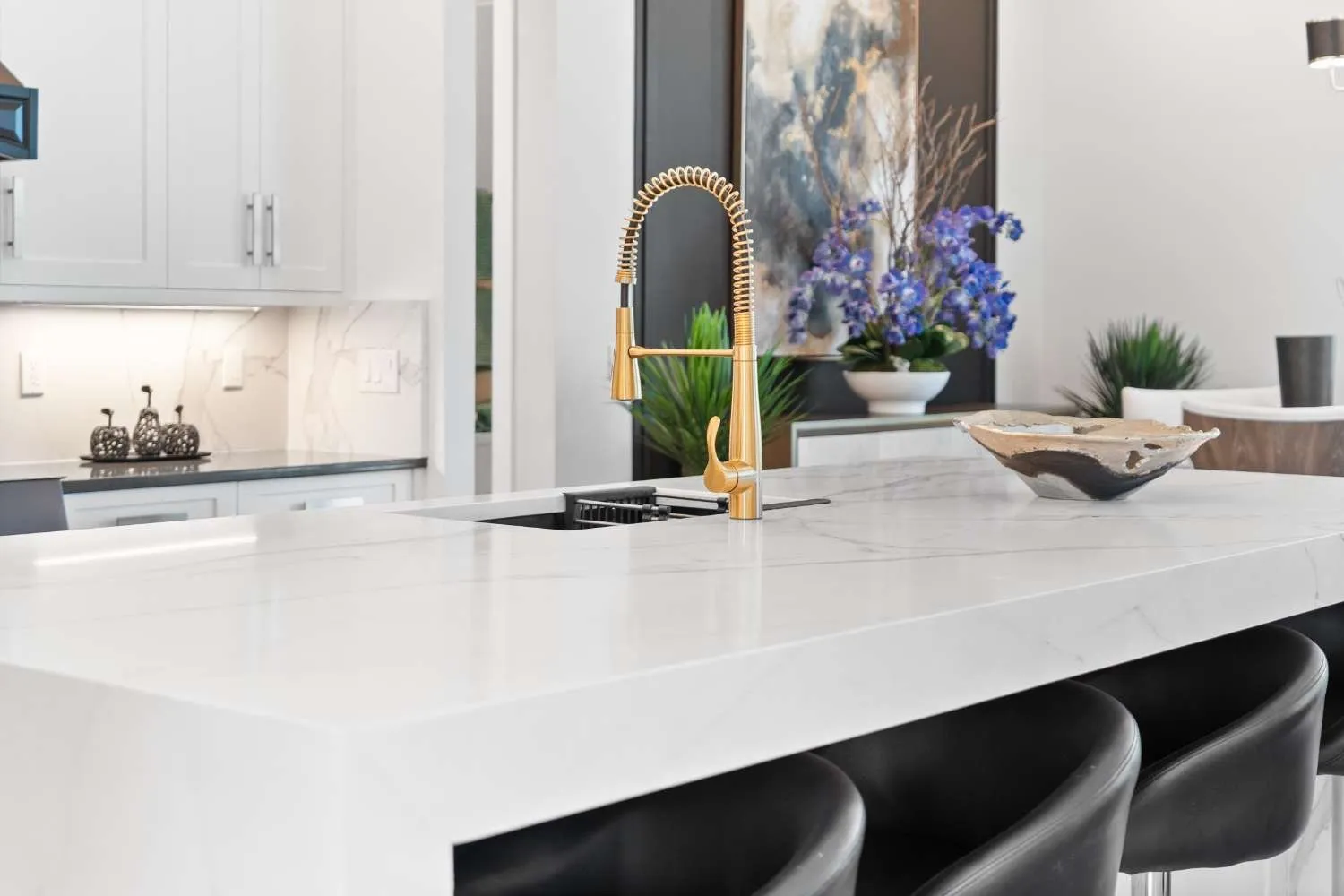 White kitchen with a quartz waterfall island and gold faucet