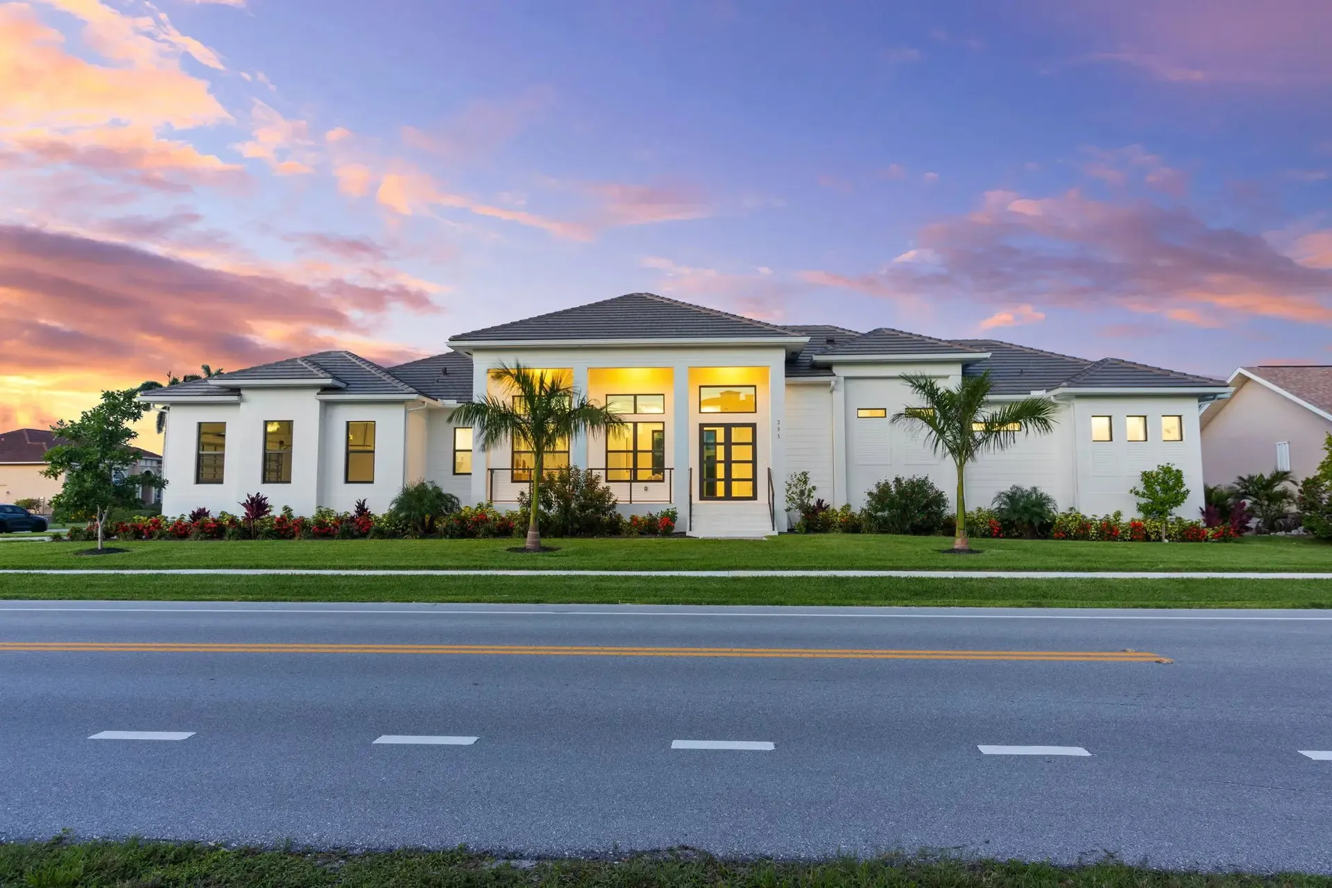 Modern white home at dusk with interior and landscape lights on