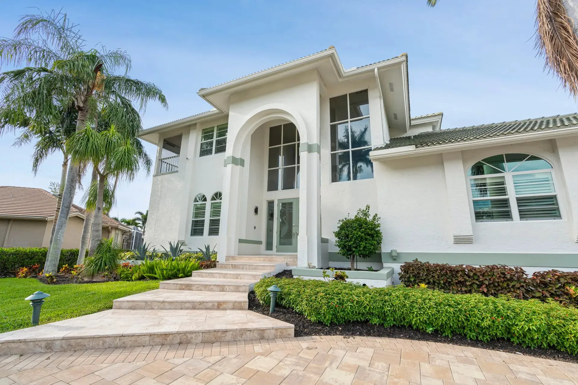 Two-story home exterior with palms and a curved walkway